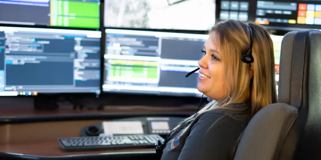 911 Telecommunicator in front of screens smiling